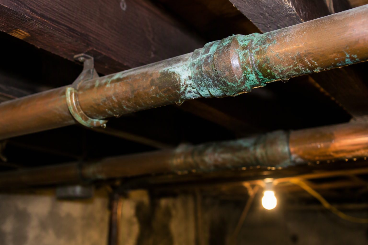 Old copper water pipes along basement joists with green corrosion at the joints